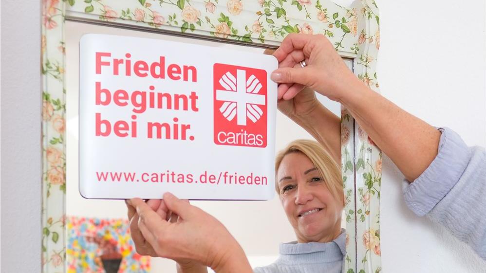 Sozialarbeiterin Christiane Emmel bringt ein Friedenaufkleber an einem Spiegel des Mädchencafés in der Beratungsstelle „No Limits“ in Hameln (Copyright: Diözesancaritasverband Hildesheim / C. Gossmann). 